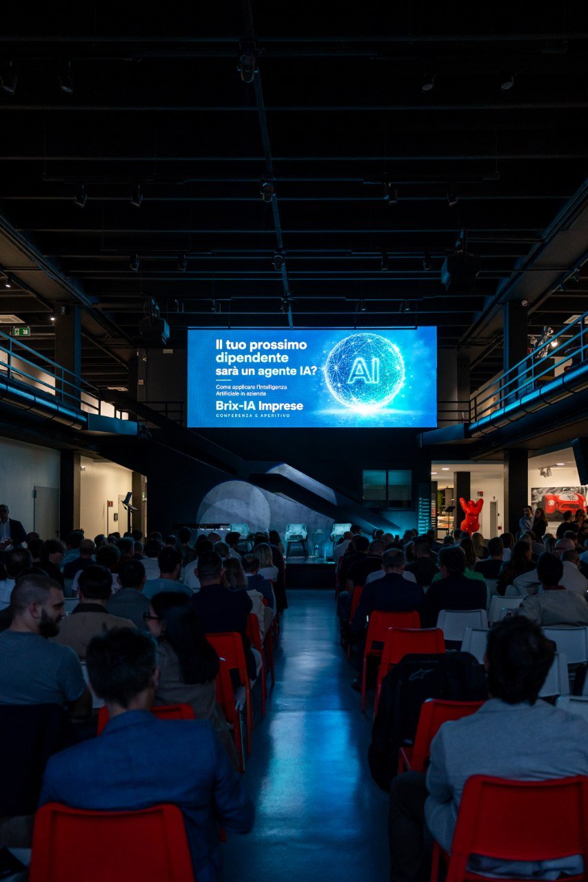 La sala di Area12 Hub gremita con lo schermo che mostra il titolo della serata Brix-IA Imprese: Il tuo prossimo dipendente sarà un agente IA?